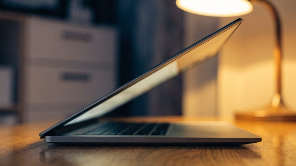 A half-closed matte grey laptop on a wooden desk
