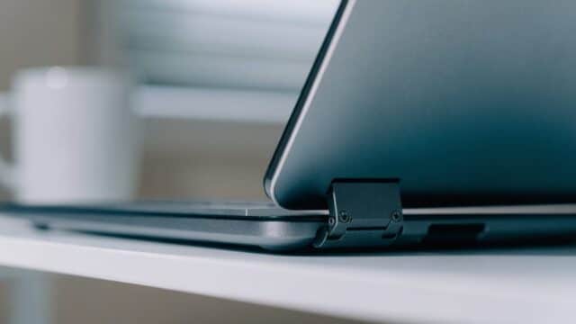 Close-up of the hinge and screen edge of a matte grey laptop on a white desk