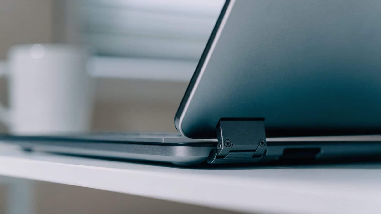 Close-up of the hinge and screen edge of a matte grey laptop on a white desk